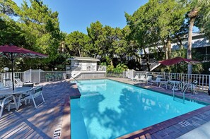 Ein Schwimmbecken mit Sonnendeck, umgeben von Bäumen und einem kleinen Gebäude.