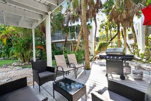 Eine Terrassengaststätte mit Korbmöbeln, einem Grill und Blick auf ein Wohngebäude.