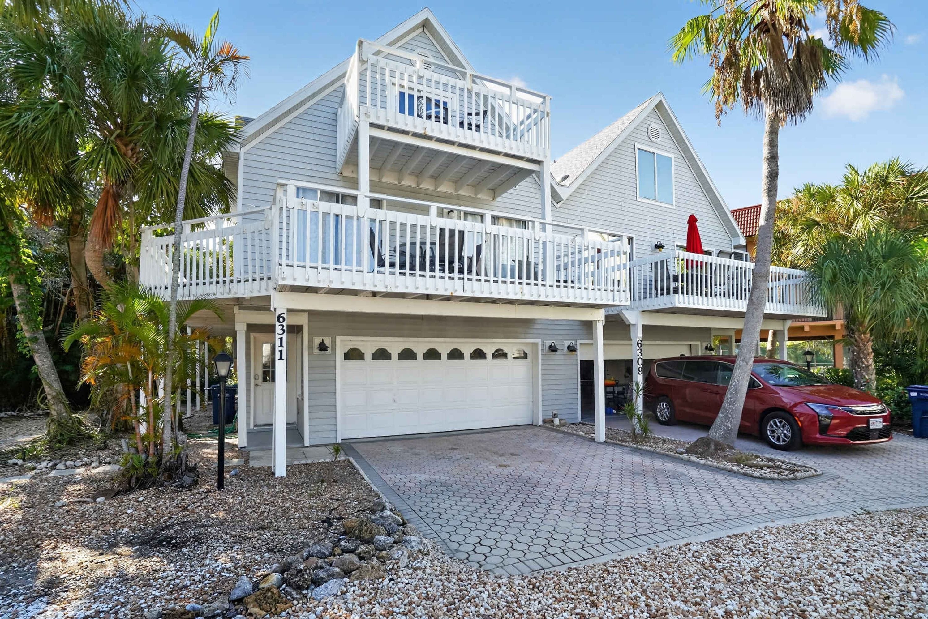 A two-story house with a balcony, a garage, and a red car parked in front.