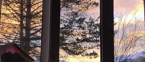 Vista a través de una ventana con un paisaje montañoso, incluyendo picos nevados y un atardecer.
