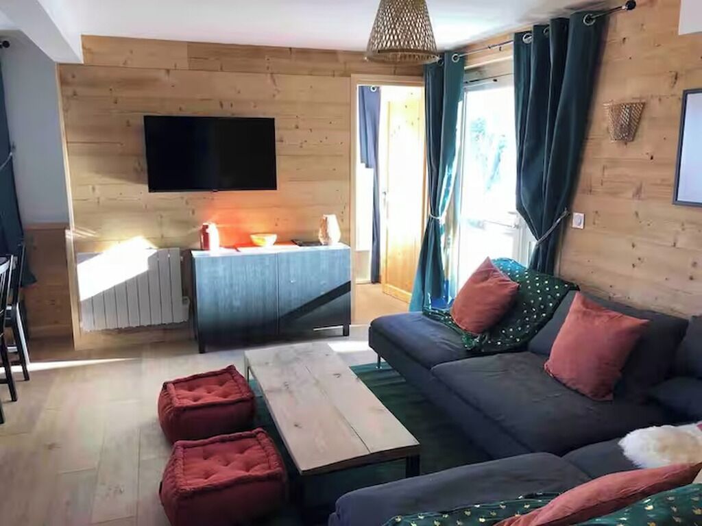 A living room with a sofa, ottomans, a coffee table, a flat-screen TV mounted on the wall, and a fireplace.