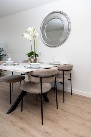 Un coin repas agrémenté d’un miroir rond au mur, une table mise avec des assiettes, des verres et un vase rempli de fleurs.