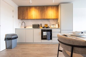 Une cuisine moderne avec des meubles blancs, une étagère supérieure en bois, un four à micro-ondes, un grille-pain et un lave-vaisselle.