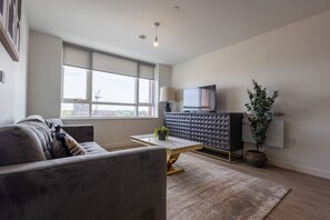 A modern living room with a sofa, a coffee table, a TV on a cabinet, and a large window. - Birmingham City Retreat No 145 (Birmingham)