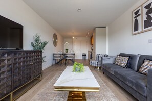 A modern living room with a flat-screen TV, a sofa, a coffee table, and a dining area with chairs and a table. - Birmingham City Retreat No 145 (Birmingham)