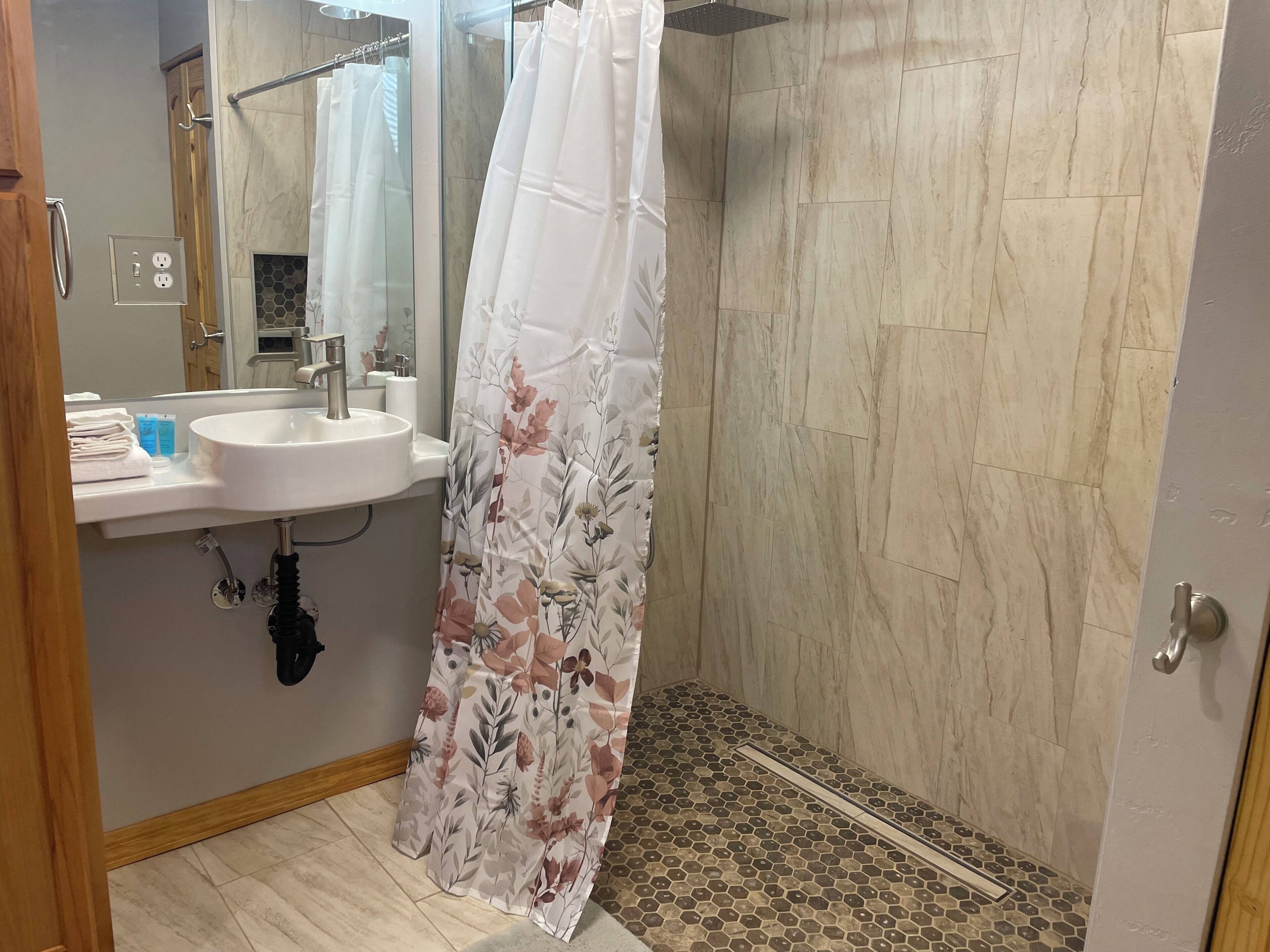A bathroom with a shower, a sink, and a mirror.