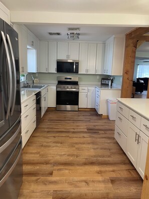 A modern kitchen with white cabinets, stainless steel appliances, and a herringbone wood floor.
