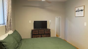 Un dormitorio con cama, cómoda, televisor, ventilador de techo y un cartel de bienvenida.