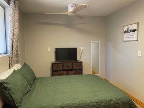 A bedroom with a bed, a dresser, a television, a ceiling fan, and a welcome sign.