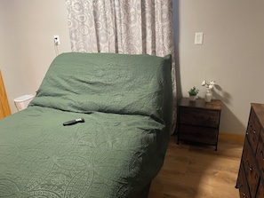 A room with a bed, a nightstand, a dresser, a power outlet, and a potted plant.