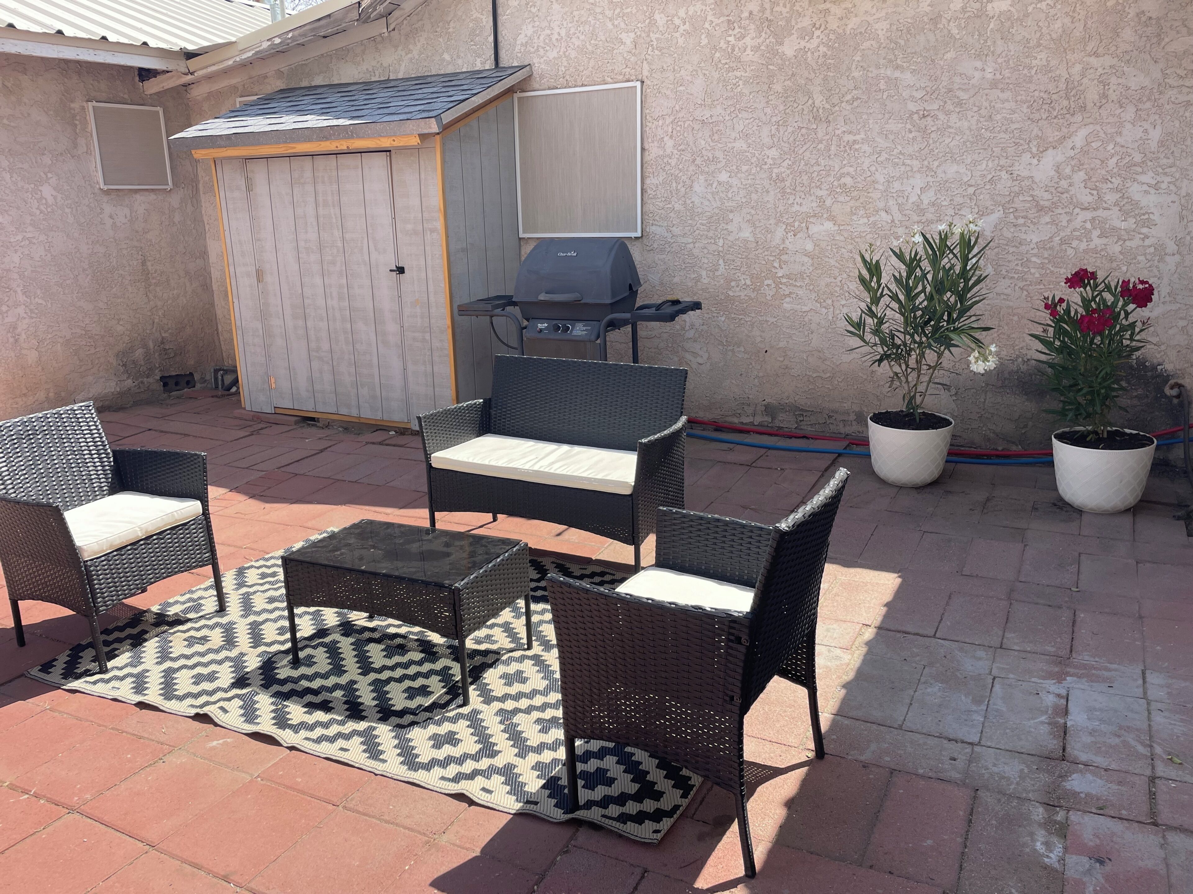 Un patio al aire libre con mobiliario de mimbre, una parrilla y plantas en macetas.