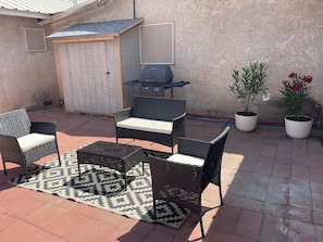 An outdoor patio with wicker furniture, a grill, and potted plants.