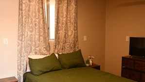 Een slaapkamer met een bed, gordijnen, een televisie en een kast.