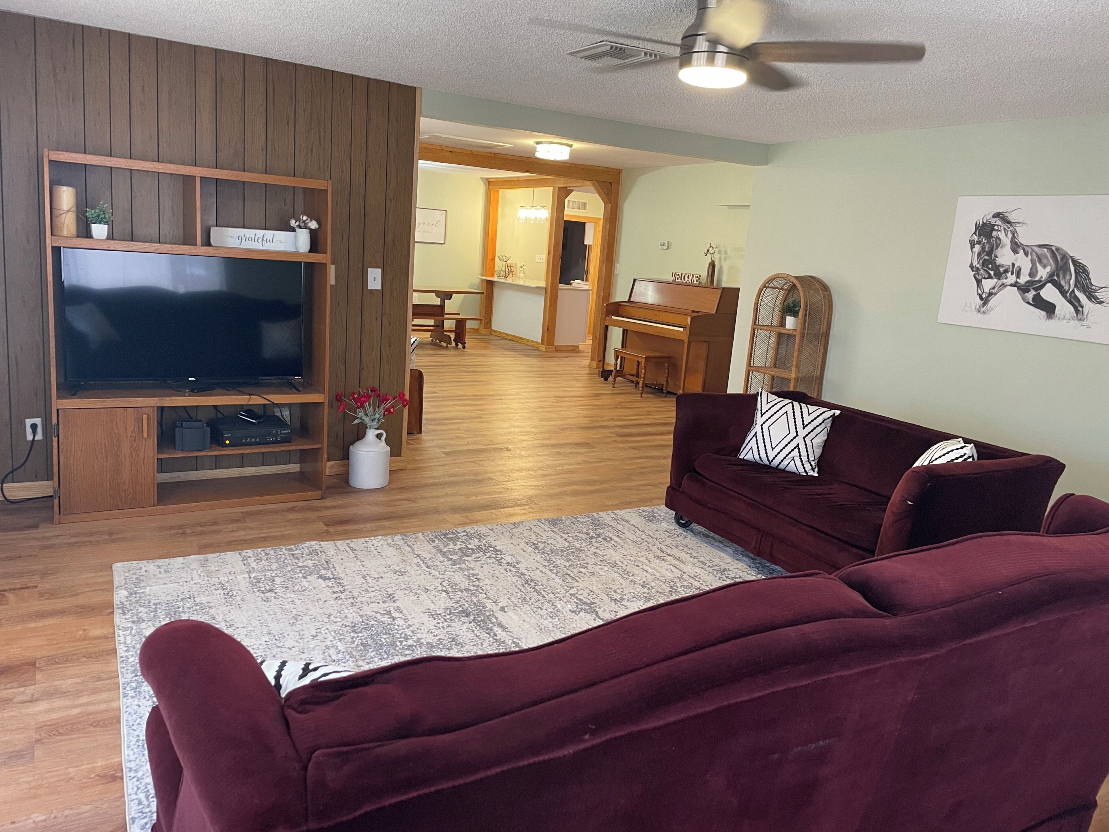A living room with a television, a sofa, a coffee table, and a piano in the background.