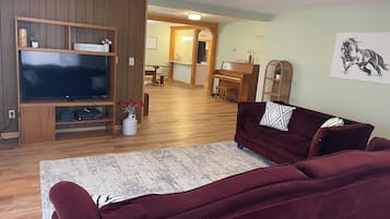 A living room with a television, a sofa, a coffee table, and a piano in the background.