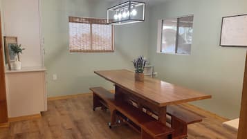 Un comedor con mesa de madera y bancos, lámpara colgante y ventana con persianas.