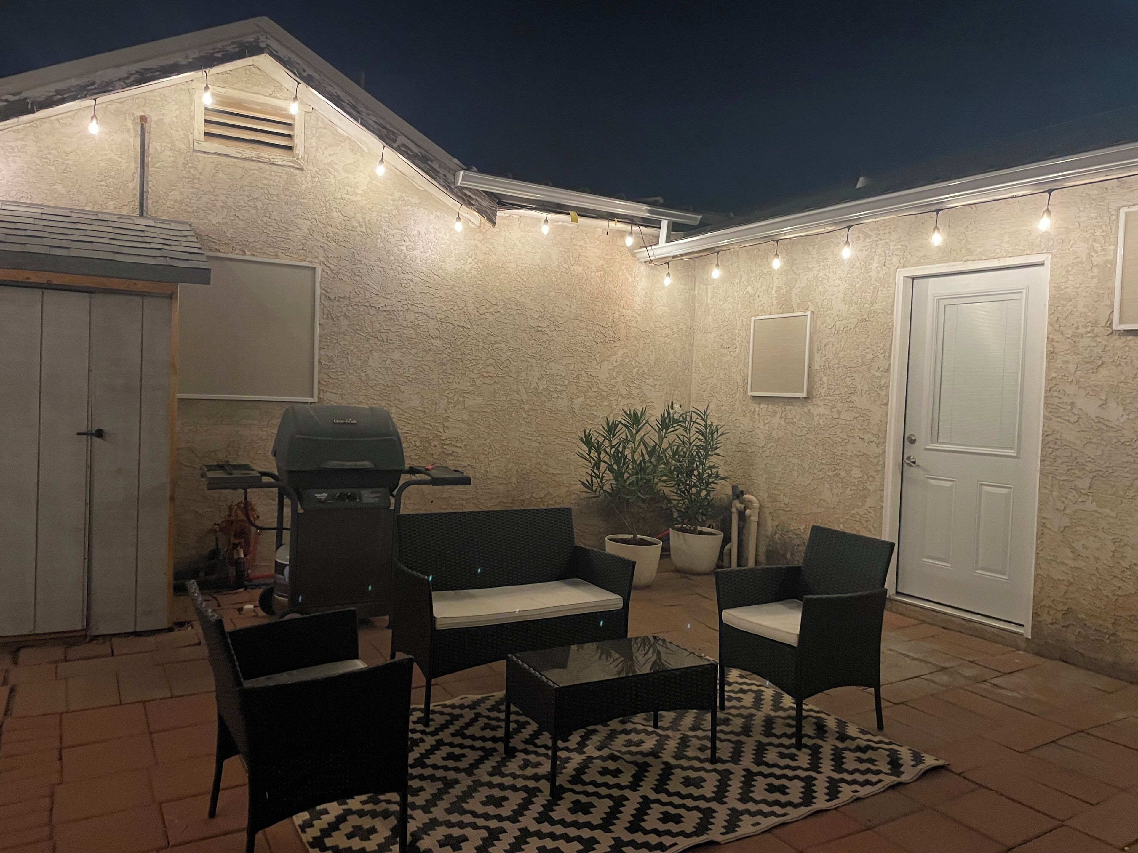 An outdoor patio with a grill, seating, and string lights.