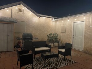 An outdoor patio with a grill, seating, and string lights.
