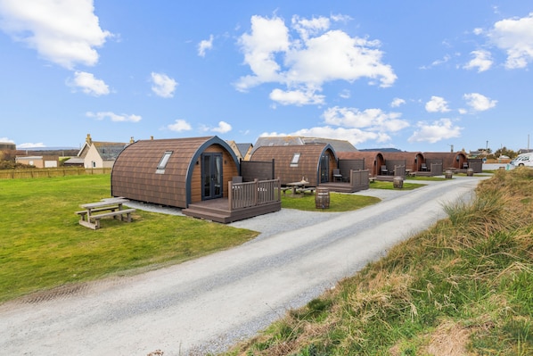 Una hilera de cabañas modernas con techos arqueados, con un camino de grava que las conecta, ubicadas en un paisaje rural.