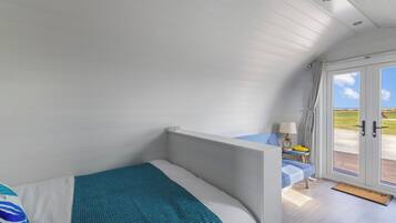 Un dormitorio con una cama, una mesita de noche con lámpara y vistas al exterior por una puerta.