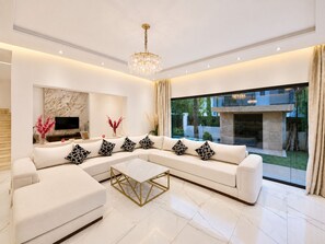 A modern living room with a sectional sofa, a coffee table, a flat-screen TV, and a large window offering a view of the outdoors. - PREMIUM EXPERIENCE - MODERN VILLA WITH EXCEPTIONAL COMFORT (مراكش)