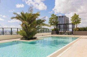 Een dakzwembad met helderblauw water, omringd door palmbomen en een modern gebouw op de achtergrond.