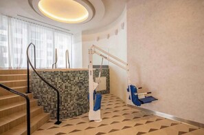 Ein Hotelbadezimmer mit Fliesenboden, einer Haltestange, einer Duschkabine und einem Fenster mit Vorhängen.