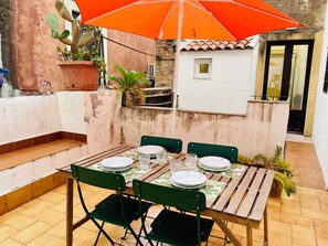 An outdoor dining area with a wooden table, green chairs, and an orange umbrella. - Fil's House—located in the historic district, close from the botanical garden (Catania)