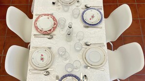 Una mesa de comedor dispuesta con sillas blancas, platos, cubiertos y vasos.