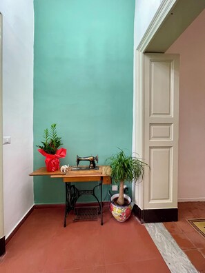 A corner room with a teal wall, a wooden table with a sewing machine, a potted plant, and a white door. - Fil's House—located in the historic district, close from the botanical garden (Catania)