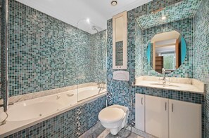 Et badeværelse med et stort badekar, et toilet og en vask med spejl.
