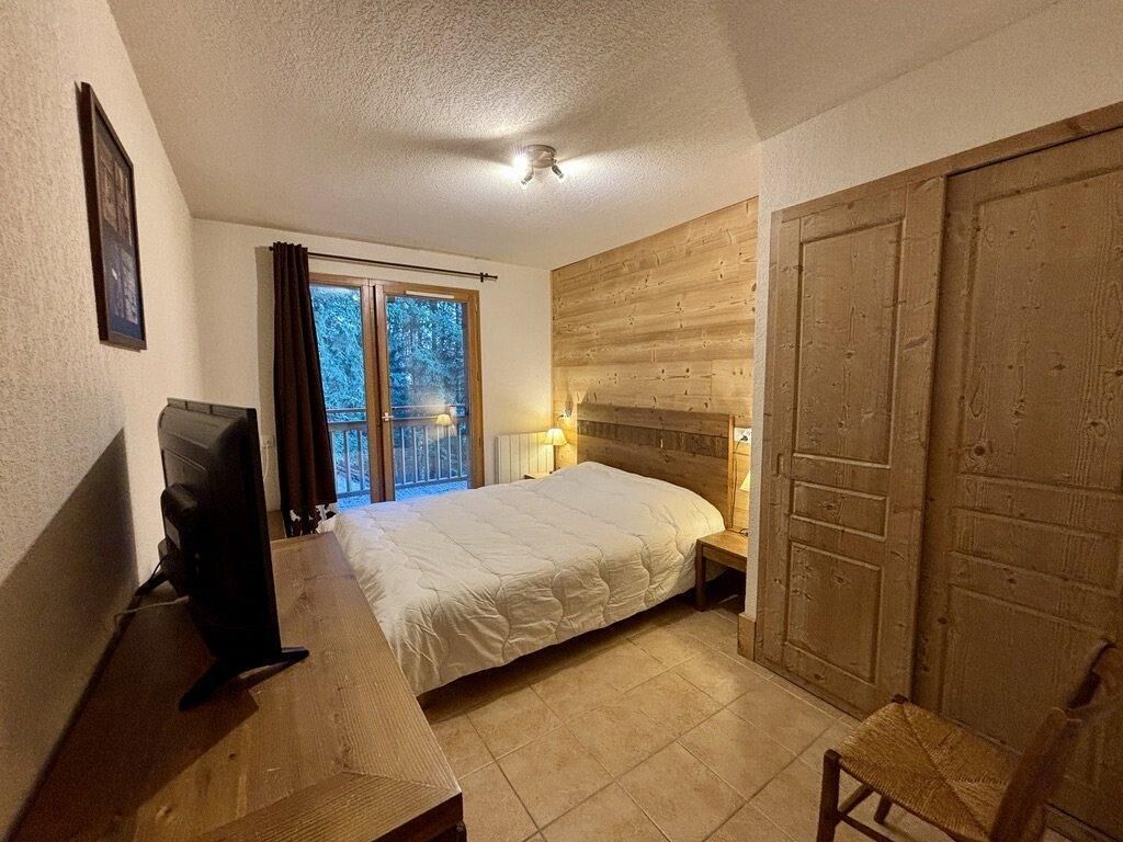 Ein Schlafzimmer mit einem Bett, einem Schreibtisch mit Computer, einem Fenster mit Vorhängen und einem Holzschrank.