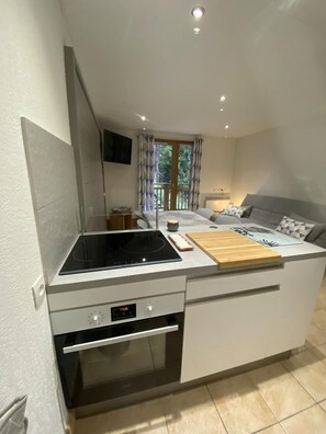 A compact kitchen with a built-in stove, a microwave, and a small oven. There is a dining area with a grey sofa and a wooden cutting board. - 150m from ski slopes, 2nd floor, balcony, tv, ski locker, 47m², Montchavin La Plagne (Bellentre)