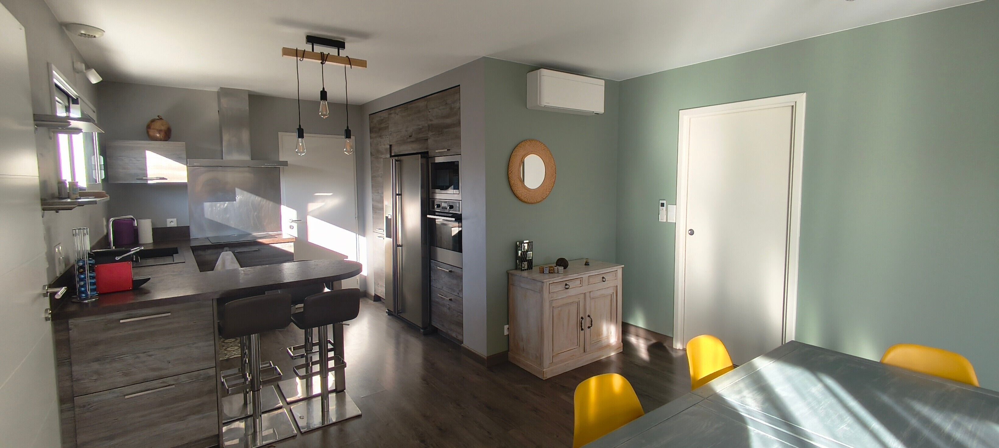 A modern kitchen with a central island, bar stools, and a dining area with yellow chairs.