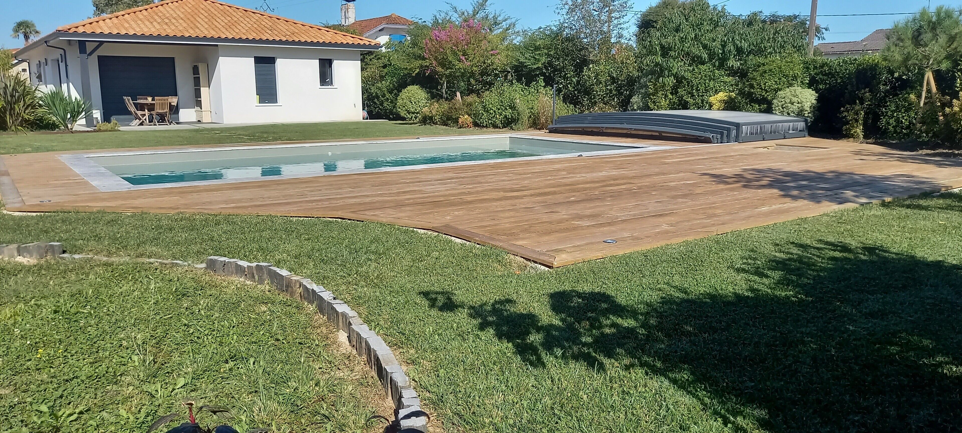 A backyard with a swimming pool, wooden deck, and a house.