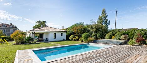 A swimming pool with a wooden deck, surrounded by a well-maintained lawn and various shrubs.
