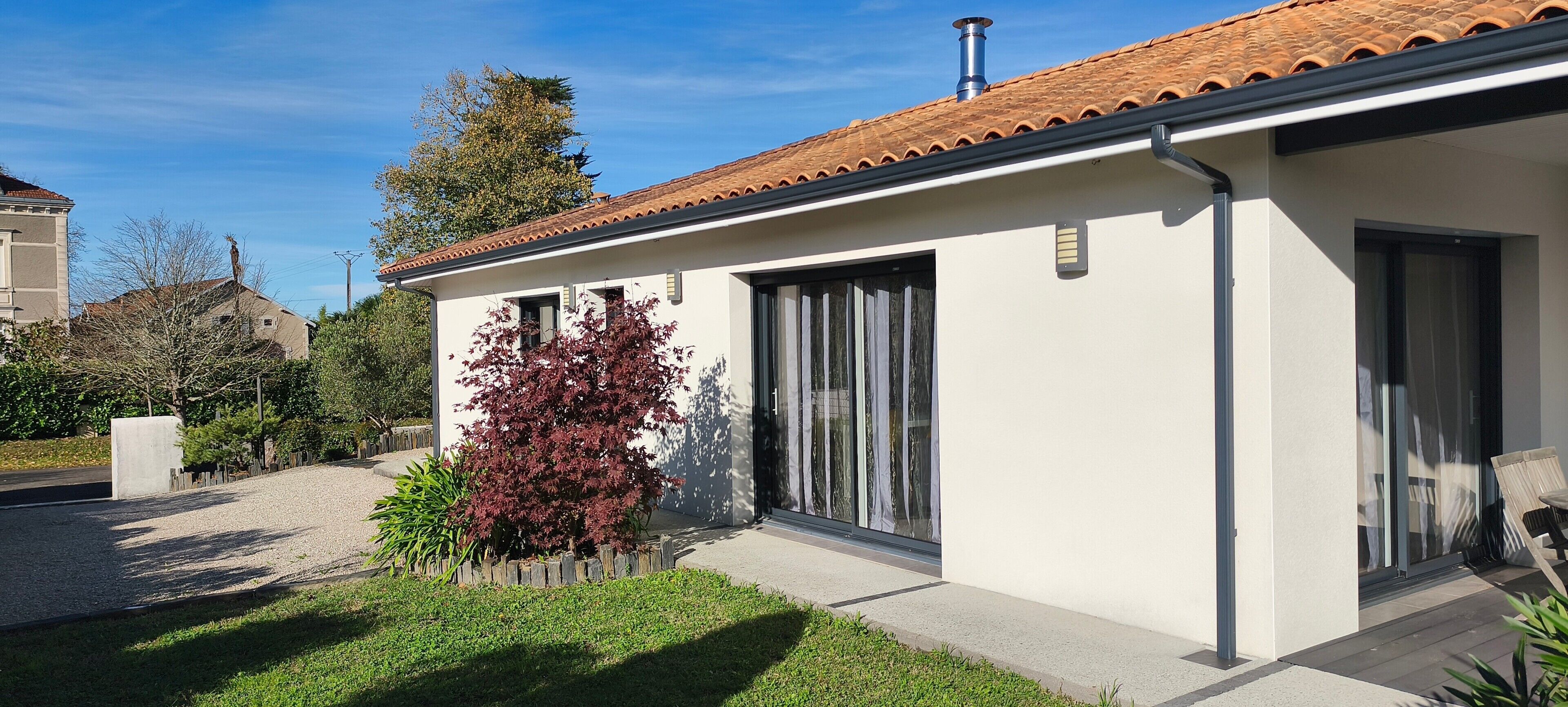 A modern house with a tiled roof, a large sliding glass door, and a well-maintained garden.