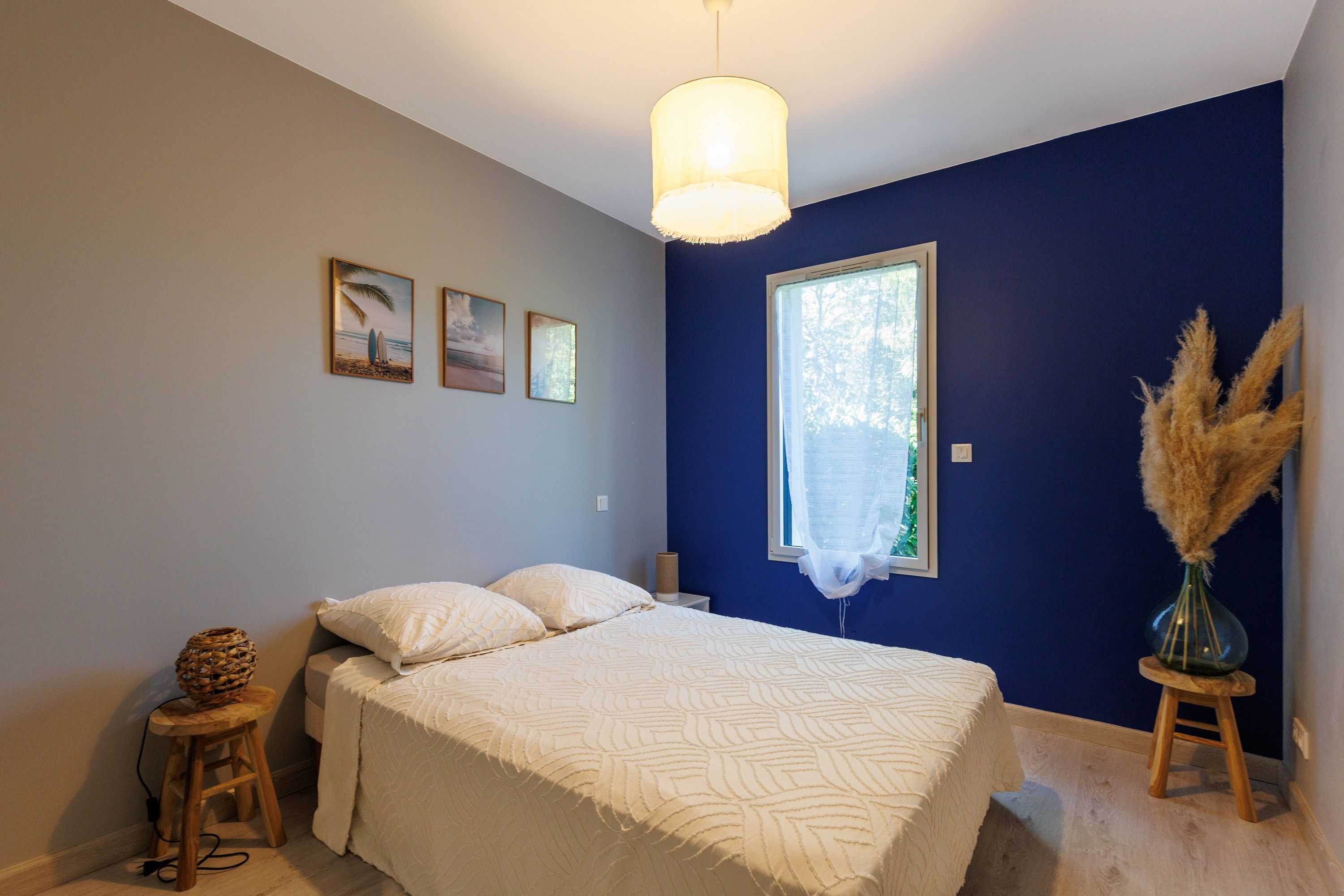 Une chambre à coucher avec un lit, une fenêtre et un mur orné de trois tableaux encadrés.