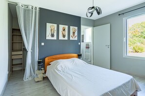 A bedroom with a bed, a wardrobe, a window, and three wall-mounted artworks.