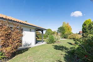 A house with a covered patio, a lawn, and various trees and shrubs.