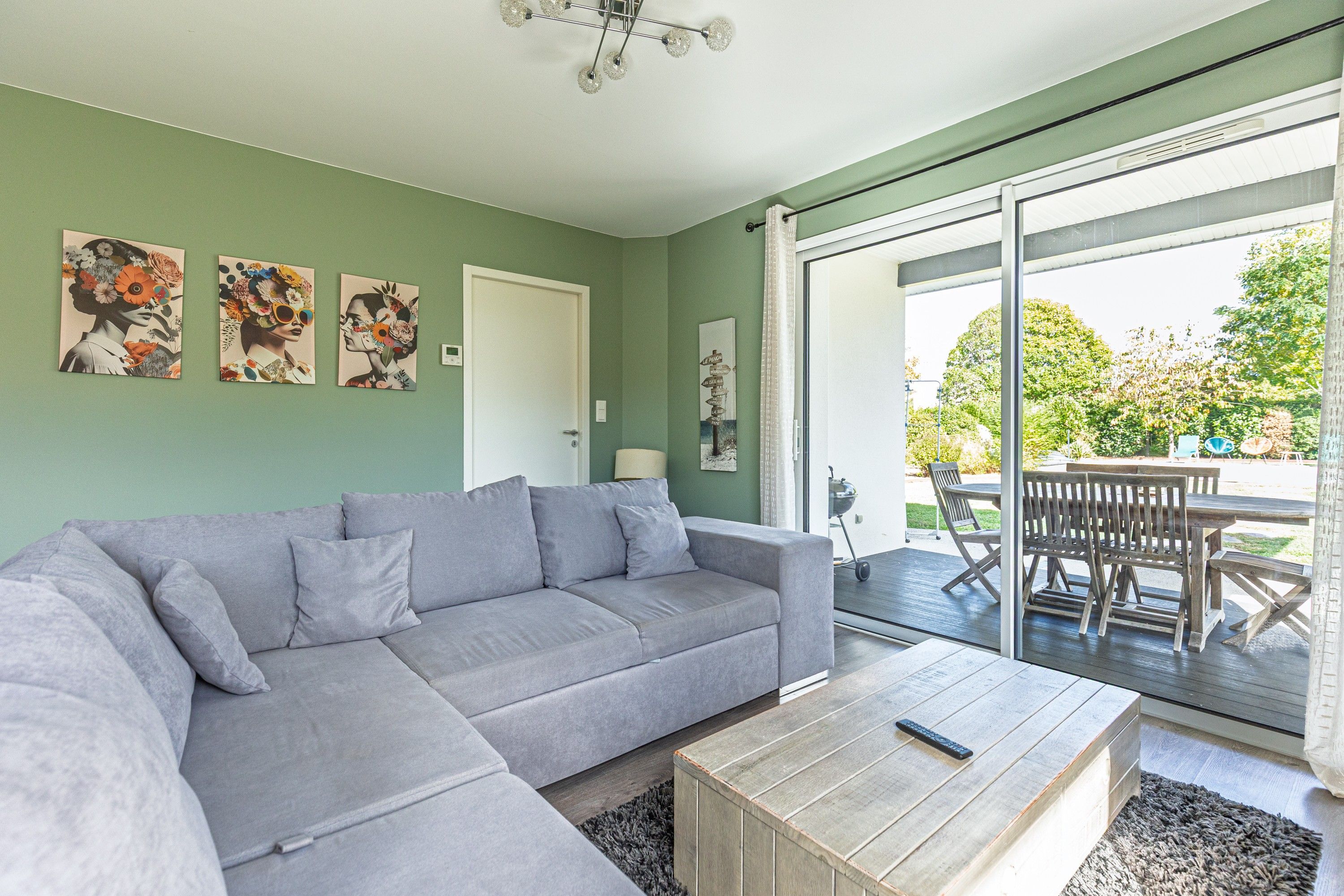 Un salon moderne avec un canapé gris, une table basse en bois et une porte-fenêtre coulissante donnant sur une terrasse extérieure.