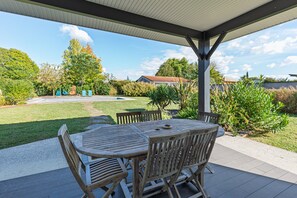 An outdoor patio with a table and chairs, surrounded by a well-maintained lawn and various plants.