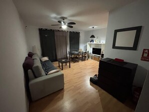 Ein Wohnzimmer mit einer Couch, einem Esstisch mit Stühlen, einem Deckenventilator und einem Fernseher.