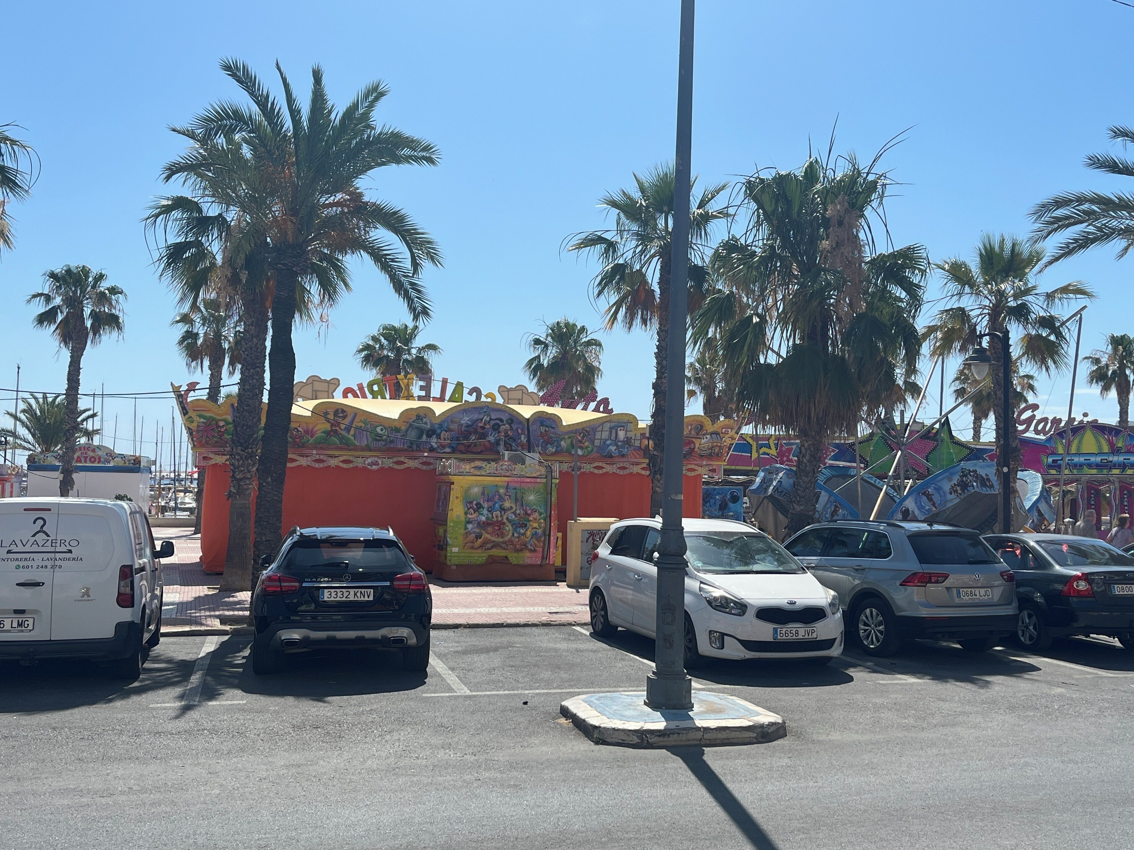 A parking lot with several cars, palm trees, and a colorful building with murals.