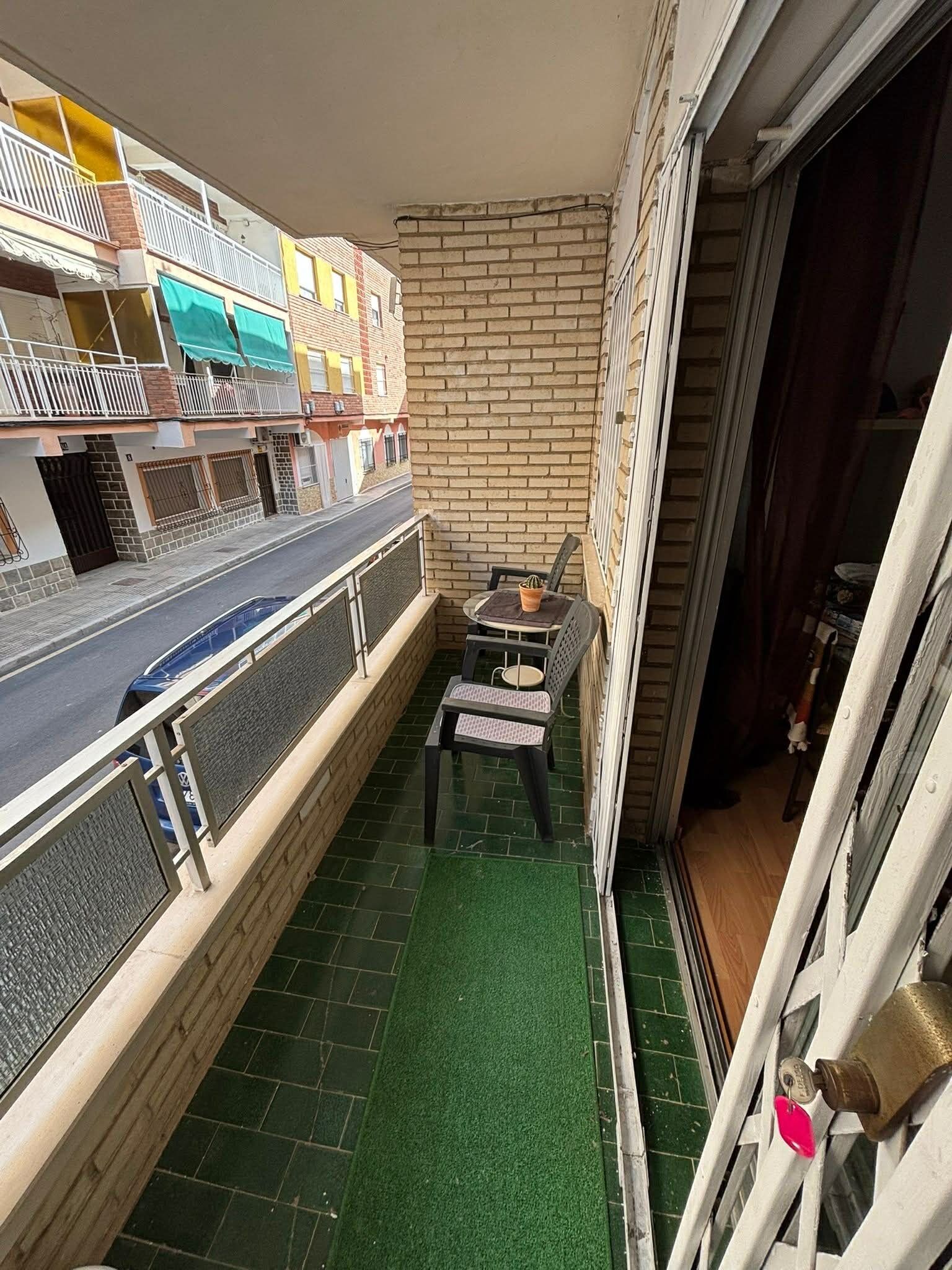 Ein Balkon mit einer grünen Matte, einem Stuhl und einem kleinen Tisch mit einer Pflanze.