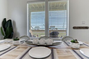 A dining area with a large window, a table set with plates and a centerpiece, and a potted plant on the side. - Family-Friendly w/ Gulf Views & Close to Beach! (Galveston)