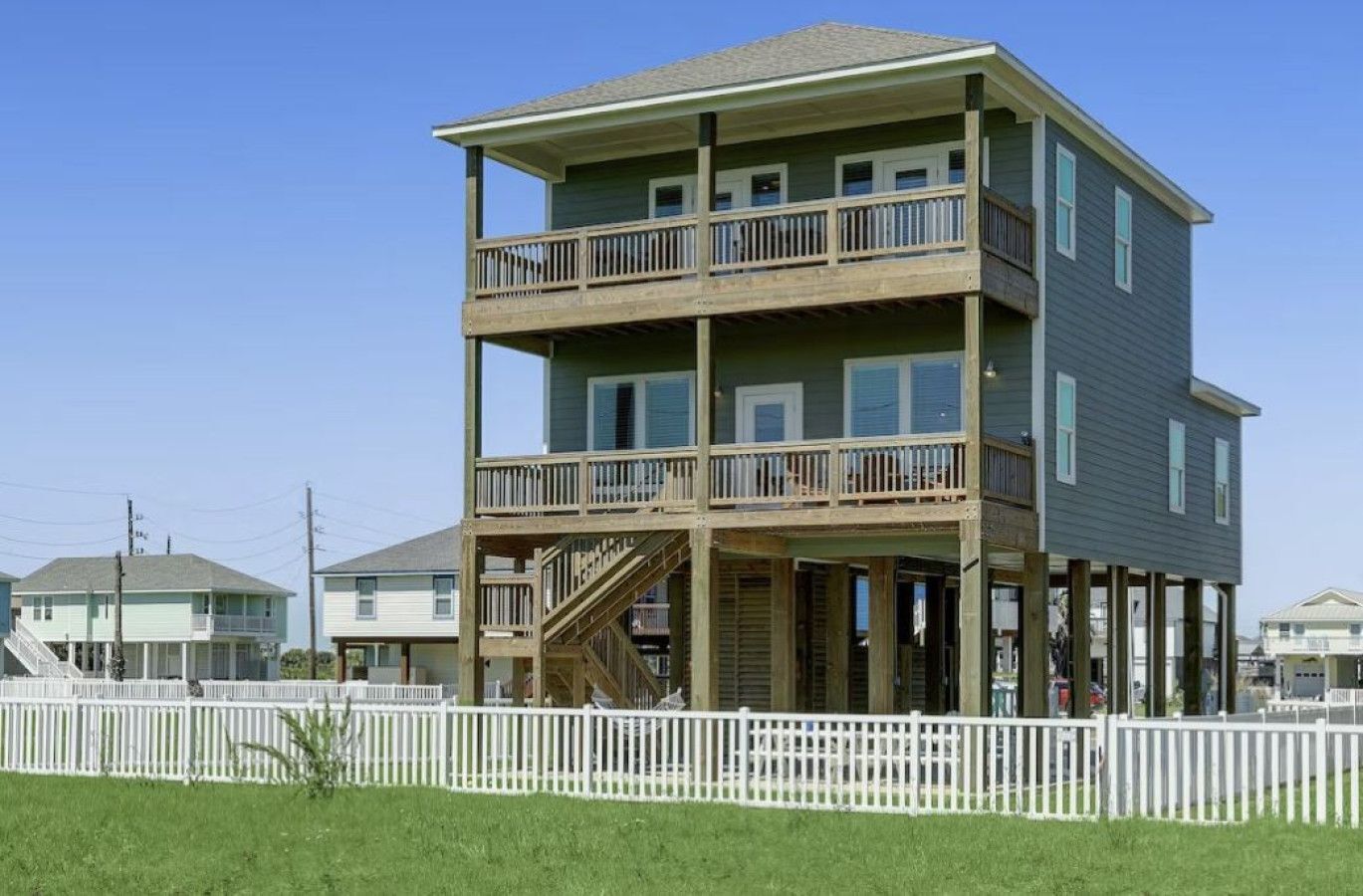 A multi-story building with a balcony on the upper level, a staircase on the ground floor, and a white picket fence in the foreground.