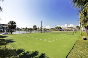 A tennis court with a net, surrounded by a fence, and a body of water in the background. - Family-Friendly w/ Gulf Views & Close to Beach! (Galveston)