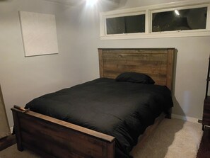 A single bed with a wooden headboard in a room with a white wall and a window above it.