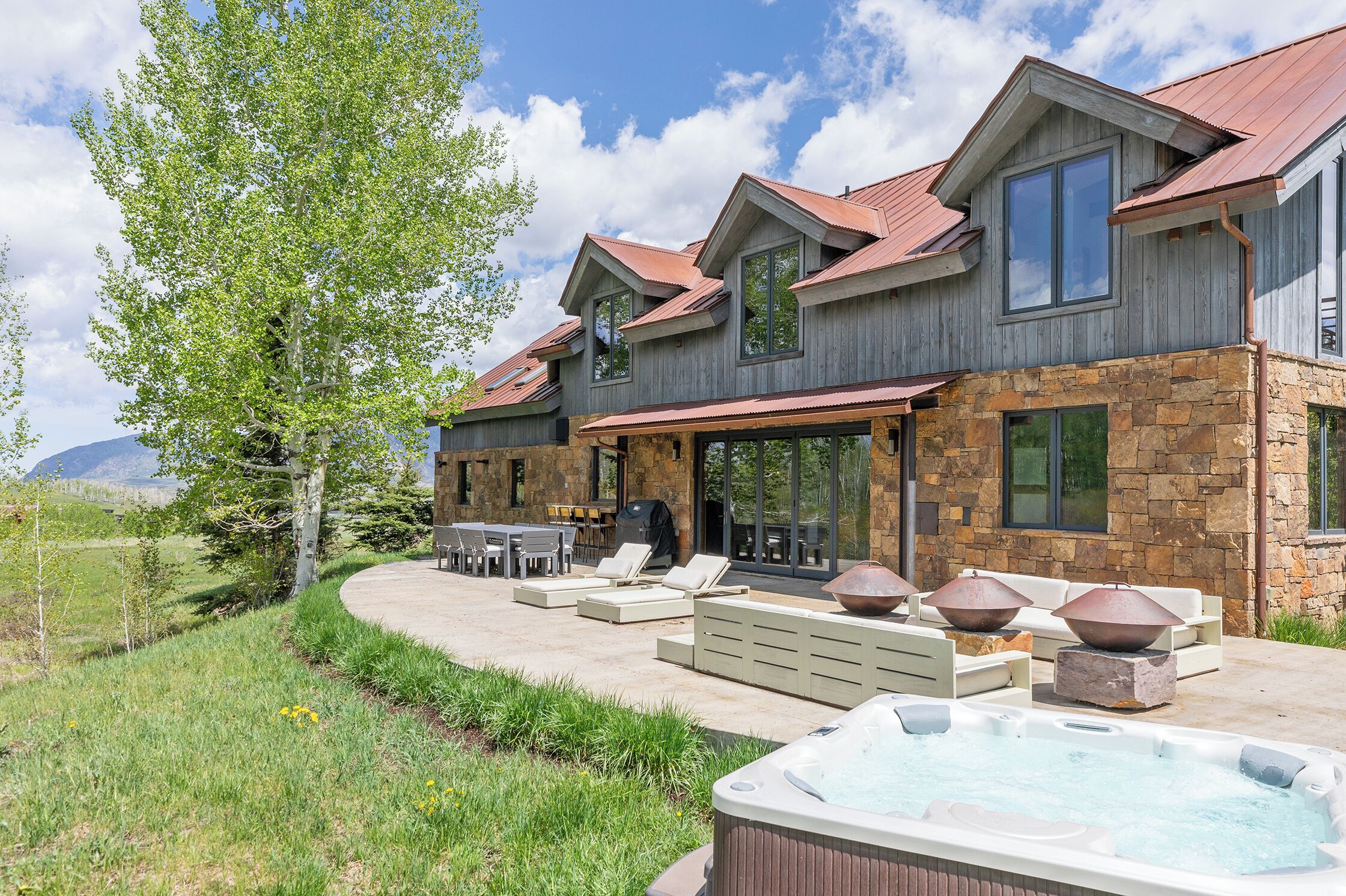 Una casa de dos pisos con fachada de piedra, un patio con mobiliario exterior y un jacuzzi.